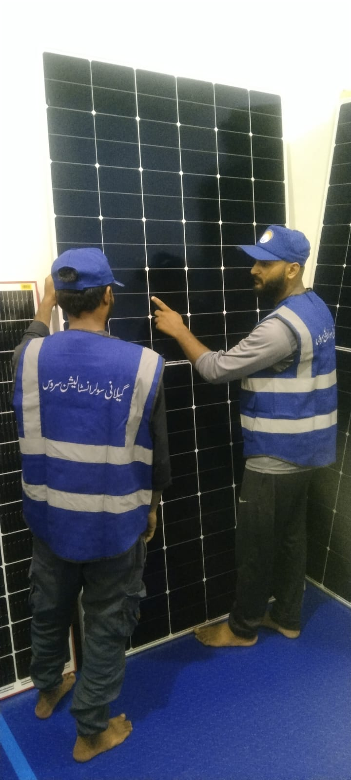 Gillani Solar team members wearing branded blue vests beside a solar panel